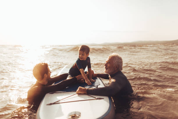 Photo of a cheerful little boy getting a surfing lessons from his father and grandfather, both experienced surfers