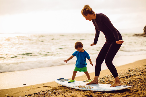 Photo of a little surfer boy and his mother (his instructor) having a surfing class on the beach by the ocean