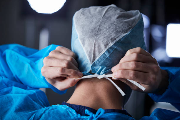Surgeon tying surgical cap in preparation, back view Surgeon tying surgical cap in preparation, back view hands tied up stock pictures, royalty-free photos & images