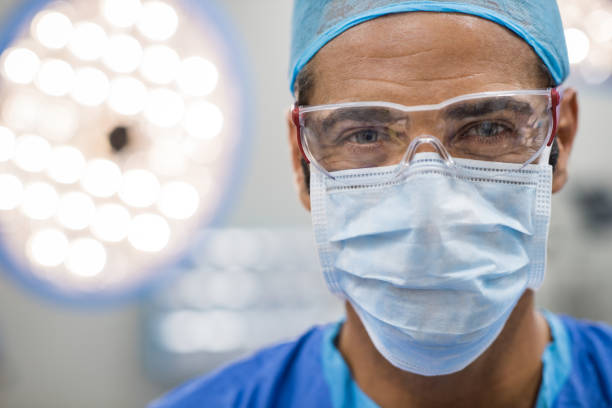 Surgeon with protective mask Close up face of surgeon man looking at camera with protective mask. Dental assistant with surgical mask and safety glasses in dental clinic. Happy successful surgeon in a operating room. surgeon stock pictures, royalty-free photos & images