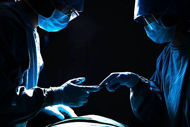 Surgeons passing surgical equipment in the operating room, dark stock photo