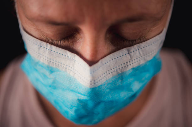 Surgical Mask Portrait of a Sad woman looking down with running tear Surgical Mask Close-up headshot portrait with a black background. A beautiful 40-44-year-old woman looking down close-up of her eyelids.  Her right eye is wet from running tears.  She is sad and emotionally distressed. south africa covid stock pictures, royalty-free photos & images