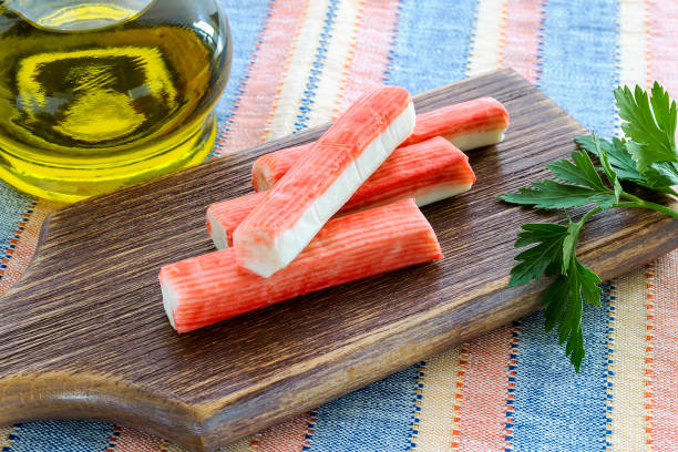 Surimi crab sticks and parsley on a brown cutting board near jar with olive oil. Seafood and ingredient for salads. Healthy eating and cook at home. stock photo