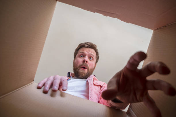 Surprised, a happy man holds out his hand trying to get a gift or parcel from an unpacked box. Unboxing inside view. stock photo