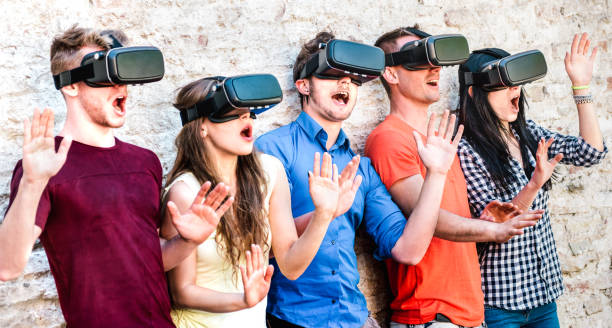 Surprised friends exploring metaverse on vr glasses - Virtual reality and wearable tech concept with happy people having fun together with headset goggles - Digital generation trends on bright filter stock photo