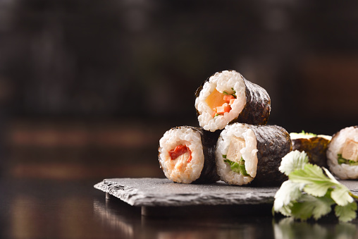 Detail of assorted sushi maki on slate plate and chopsticks on black wooden table. Front view. Horizontal composition.