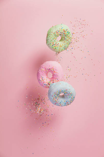 Sweet and colourful doughnuts with sprinkles falling or flying in motion Sweet and colourful doughnuts with sprinkles falling or flying in motion against pastel pink background sugar food stock pictures, royalty-free photos & images