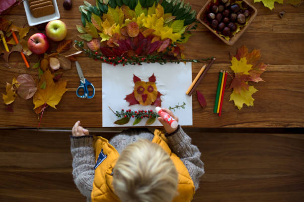 Sweet child, boy, applying leaves using glue while doing arts and chraft with leaves stock photo