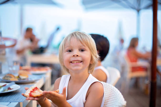 Sweet child, cute boy, eating pizza and french fries in a restaurant on the beach stock photo