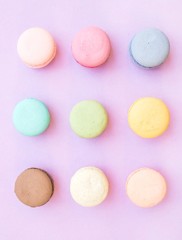 Sweet colorful French macaroon biscuits on pastel lilac background, top view