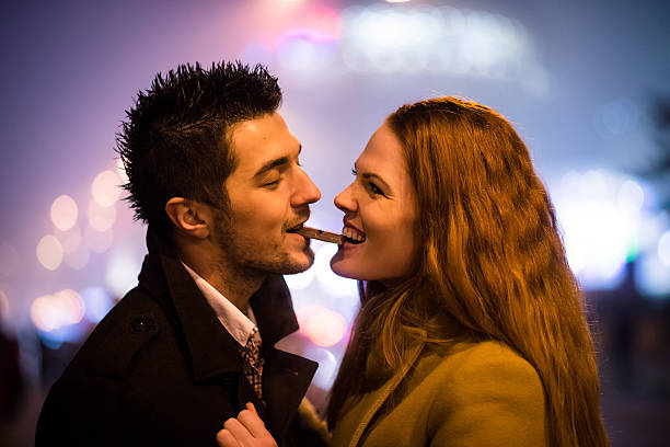 Sweet date - couple eating chocolate Couple eating together one piece of chocolate in street at winter night couple eating chocolate stock pictures, royalty-free photos & images