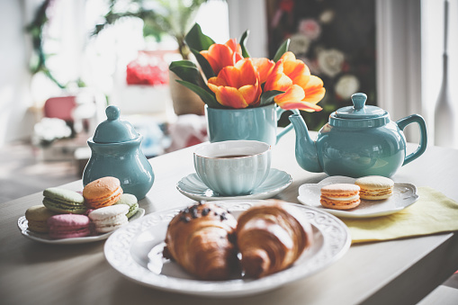 Tea cup, tea pot, macaroons, croissants and tulips on the coffee table.