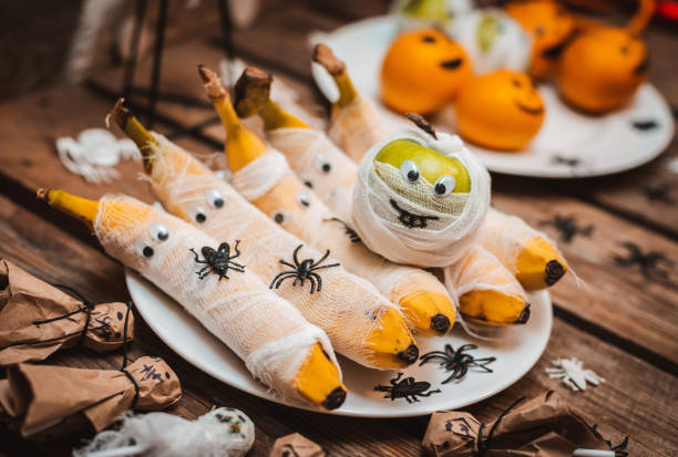 Sweet table with fruits and treats for Halloween. Decorations Apple bananas in the form of a mummy with eyes and Ghost. spiders and cockroaches stock photo