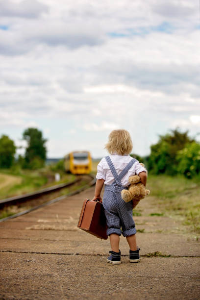 oyuncak ayı, kitap ve vintage bavul ile tatlı yürümeye başlayan çocuk bir tren istasyonunda tren bekliyor - teddy ray stok fotoğraflar ve resimler