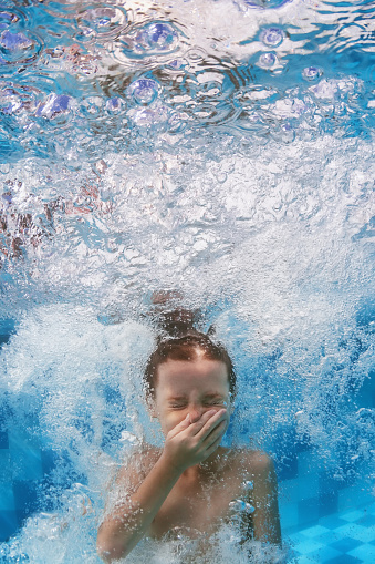 Funny face portrait of boy swimming and diving in blue pool with fun - jumping deep down underwater with splashes and foam. Family lifestyle and summer children water sports activity with parents