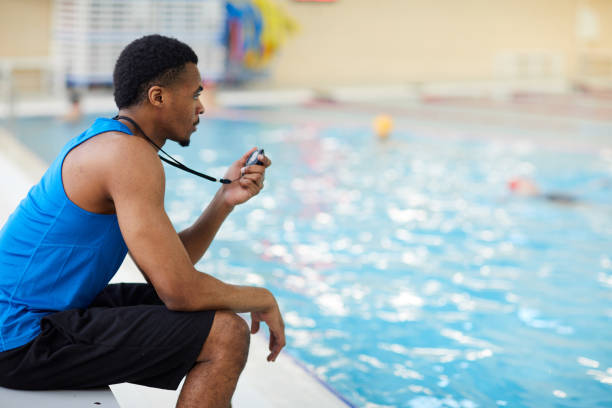 Swimming Pool Guard on Duty Side view portrait of handsome African-American fitness coach working in swimming pool, copy space lifeguard stock pictures, royalty-free photos & images