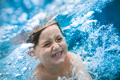 Close up of young boy swimming underwater. Bubbles are all around him.