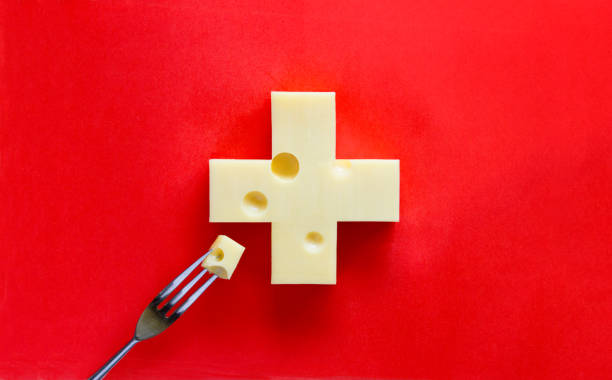 Swiss cross in form of cheese on red background, with a piece on fork stock photo