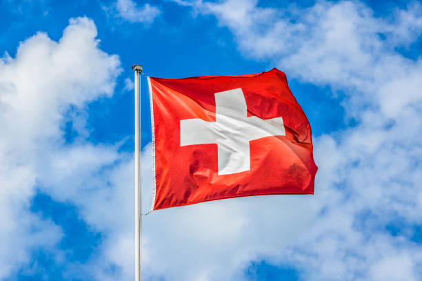 Swiss flag waving in the wind on a sunny day with blue sky and clouds stock photo