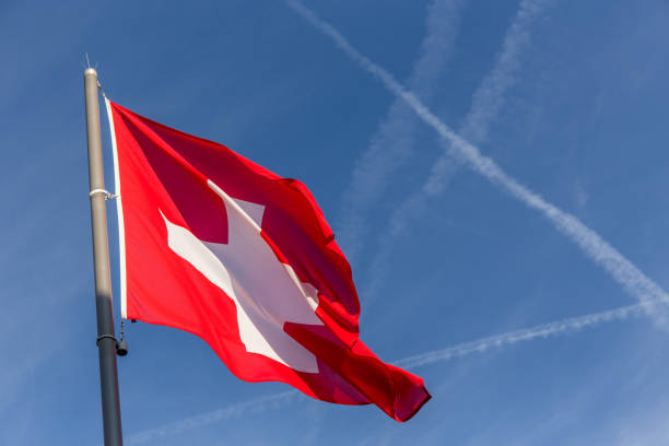 switzerland flag waving with crossing flight trail on blue sky background in summer day and copy space stock photo