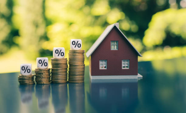 Symbol for increasing interest rates. Dice with percentage symbols on increasing high stacks of coins next to a model house. stock photo