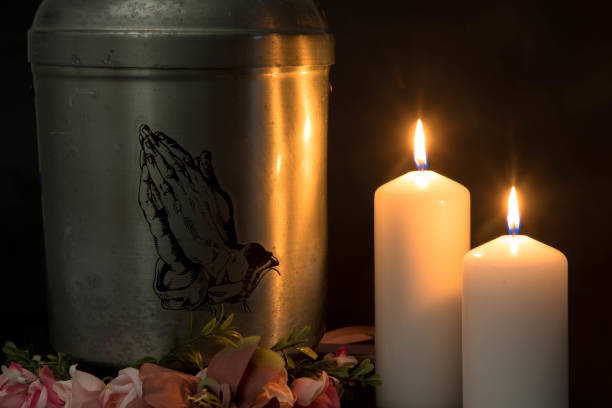 Sympathy card. Funeral urn with praying hands and burning candles. Metal urn with ashes of a dead person on a funeral. Sad grieving moment at the end of a life. Last farewell and grief concept. End of Life funerary urn stock pictures, royalty-free photos & images