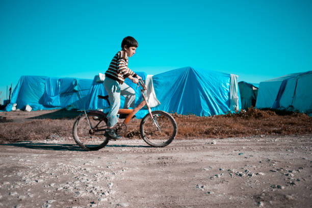 сирийский маленький мальчик в лагере беженцев на велосипеде - migrants стоковые фото и изображения