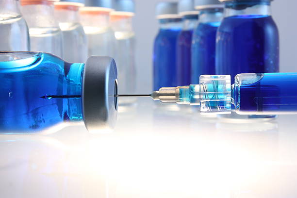 Syringe with blue liquid entering bottle with more behind stock photo