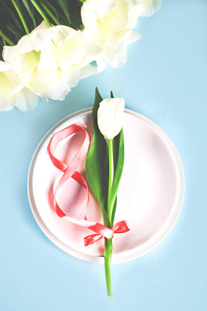 Table setting with white tulip on the plate. Spring 8 march concept. International Women's Day. Top view. stock photo
