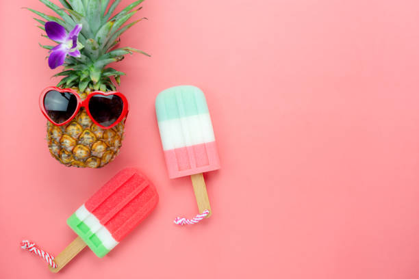 Table top view aerial image of summer & travel beach holiday in the season background concept.Flat lay sign objects food on season for travel.pineapple wear sunglasses with ice cream on pink paper. stock photo