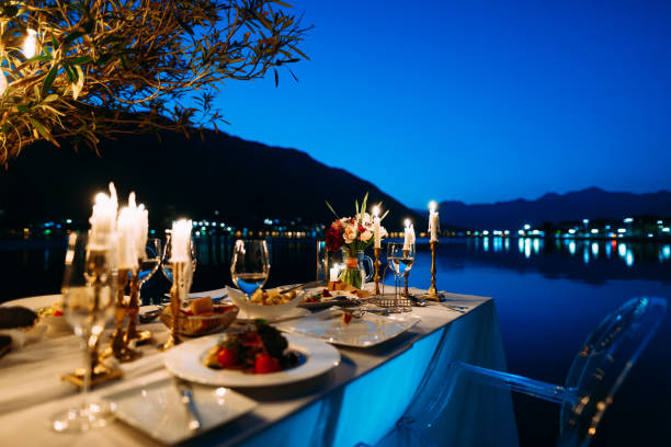 een lijst met diner voor twee, een boeket van bloemen en kaarsen tegen de achtergrond van water en bergen in de avond, in een restaurant in de stad kotor, montenegro. - sunset dining stockfoto's en -beelden