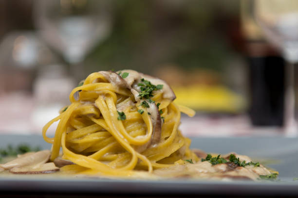 Tagliatelle with mushrooms Close up on a restaurant table with a dish of italian pasta, tagliatelle with porcini mushrooms. Background is blurred, no people are visible in the frame. tagliatelle stock pictures, royalty-free photos & images