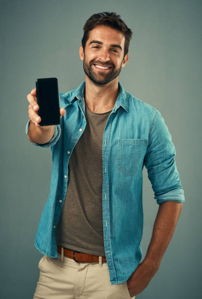 Take a look and tell me what you think Studio portrait of a handsome young man holding a cellphone with a blank screen against a grey background showing stock pictures, royalty-free photos & images