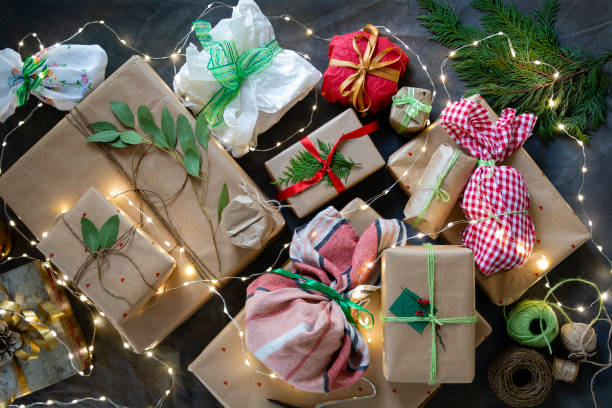 Take Your Pick! An overhead view of wrapped Christmas presents on a backdrop which have been decorated with ribbon, string, eucalyptus leaves and holly leaves. They are ready to be given at Christmas time and they are on the table, draped in Christmas lights. customised gift stock pictures, royalty-free photos & images
