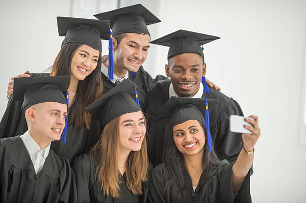 Taking a Selfie After Graduation A multi-ethnic group of college age graduates are standing together in a group and are taking a selfie on a cell phone camera. phd programs online stock pictures, royalty-free photos & images
