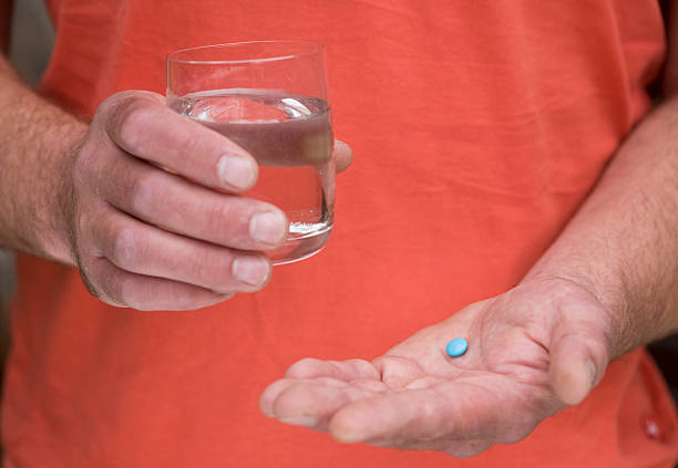 Taking blue tablets pills and a man holding a glass of water in his hand anti impotence tablet stock pictures, royalty-free photos & images
