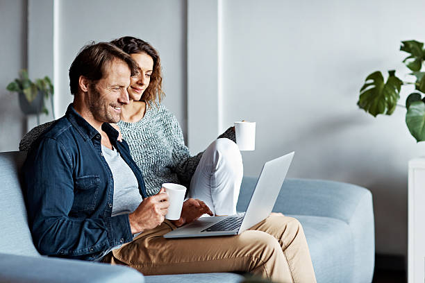 Taking it easy on the sofa Shot of a mature couple sitting on their sofa using a laptop mid adult couple stock pictures, royalty-free photos & images