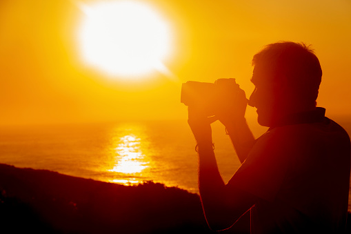 Silhouette of people taking photos at sunrise with a cell phone and DSLR camera