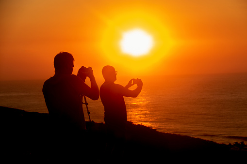 Silhouette of people taking photos at sunrise with a cell phone and DSLR camera