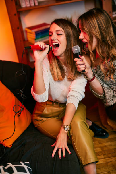 Talented girls with beautiful voices sit at home and sing a duet at karaoke night. stock photo