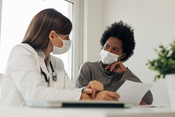 Talking about patients diagnosis. Both of these woman wearing mask, doctor and patient. woman talking to doctor stock pictures, royalty-free photos & images