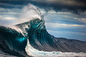 istock Tall powerful cross ocean wave breaking during a dark, stormy evening. 1368262606
