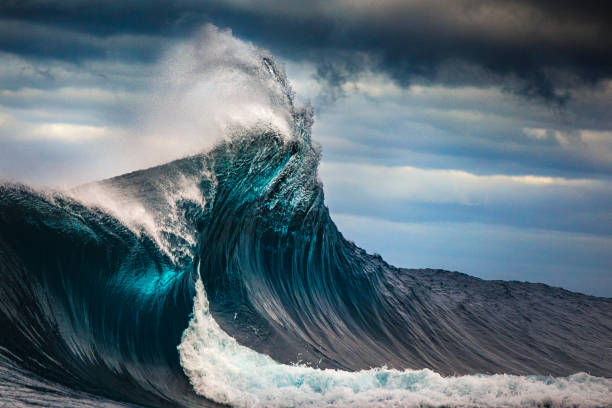 Tall powerful cross ocean wave breaking during a dark, stormy evening. stock photo