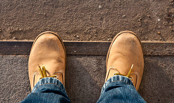 Tan-colored workman's boots up close with blue jeans stock photo