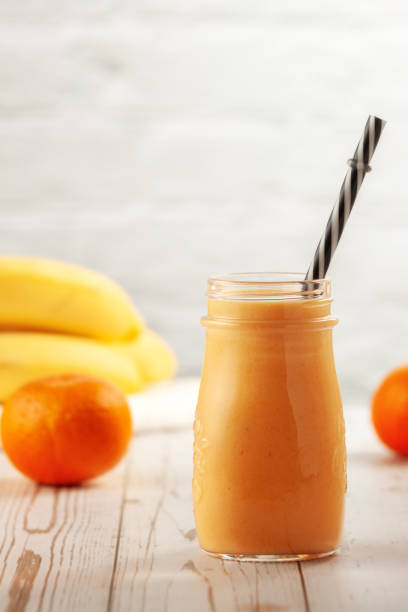 Tangerine and banana smoothie on wooden table On a wooden table in bottles is a tangerine-banana smoothie orange smoothie stock pictures, royalty-free photos & images
