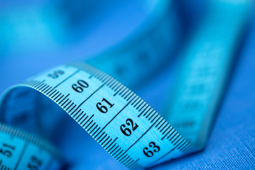 Close-up of tape measure on a green background. Shallow depth of field, space for copy.