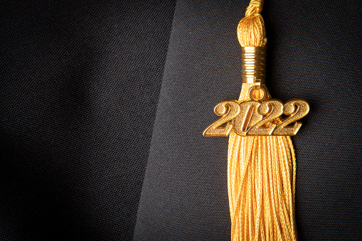 A gold colored tassel with a 2022 charm on it on a black background.