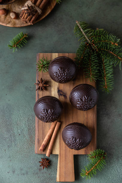Tasty cocoa bombs with marshmallow and chocolate on wooden plate with fir branches and spices. Trendy winter hot drink. Top view. stock photo