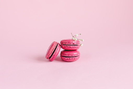 Tasty french macaroons with small white flower on a pink pastel background. Place for text.