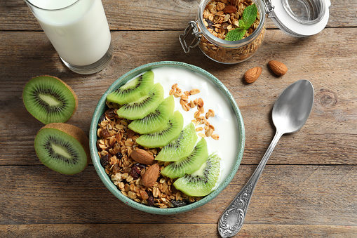 Tasty granola with yogurt and sliced kiwi served for breakfast on wooden table, flat lay